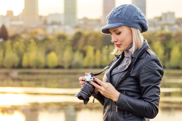 Femme blonde élégante en bleu béret français photographe prend des photos de la forêt d'automne au coucher du soleil