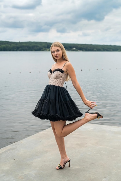 Femme blonde élégante dans une robe de nuit noire fashion près du lac lifestyle