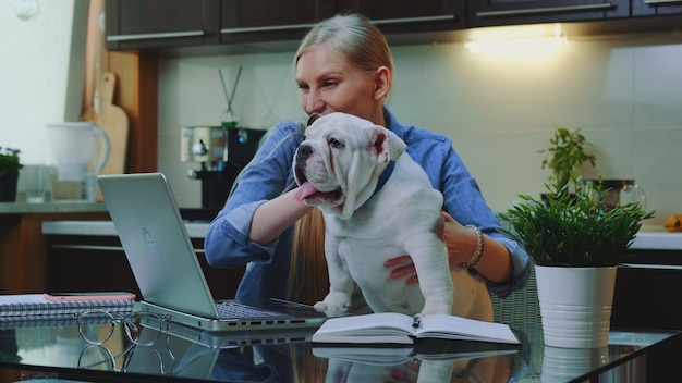 Femme blonde faisant un appel vidéo en ligne à ses proches pour montrer un petit bulldog