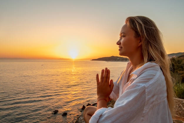 Photo femme blonde faisant de l'exercice de pranayama de respiration sur le coucher du soleil sur la mer. .