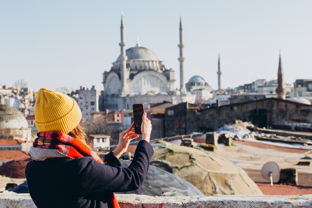 Photo femme blonde fait une photo sur le téléphone sur le toit du grand bazar, istanbul, turquie. fille au chapeau jaune prend un selfie sur une journée d'automne ensoleillée. fille de voyageur marche à travers l'hiver istanbul.