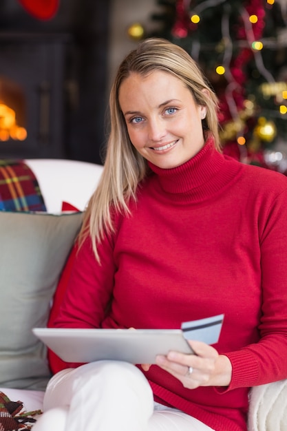 Femme blonde festive en utilisant sa carte de crédit et tablet pc