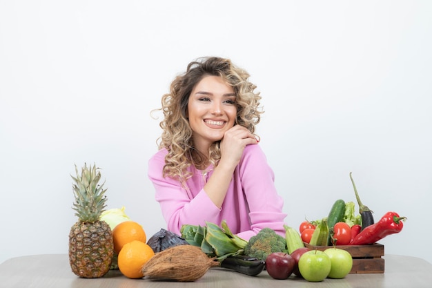 femme blonde en haut rose assis à table avec de nombreux fruits.