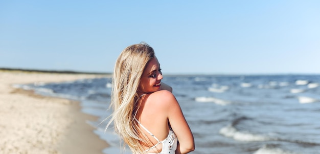 Une femme blonde heureuse dans le bonheur libre sur la plage de l'océan debout droit et posant