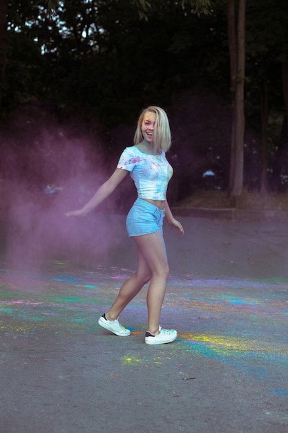 Femme blonde heureuse avec de la peinture sèche qui explose célébrant le festival Holi