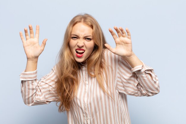 Femme blonde hurlant de panique ou de colère, choquée, terrifiée ou furieuse, avec les mains à côté de la tête