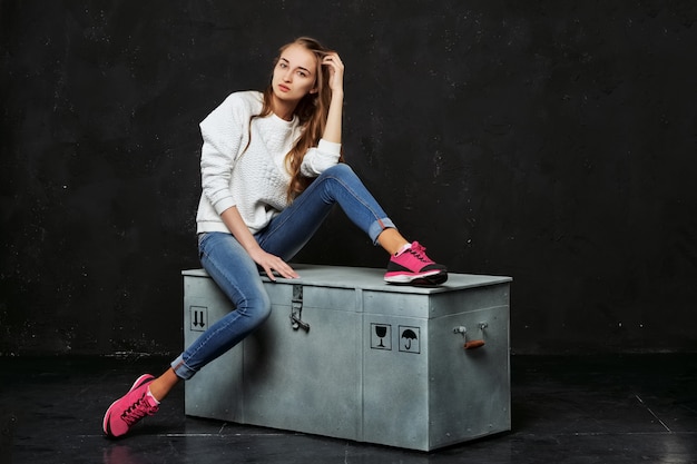 Femme blonde en jeans et baskets roses assis sur une boîte à colis