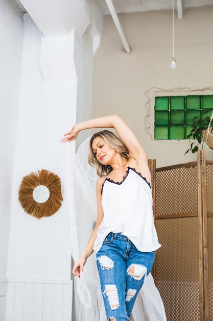 Femme blonde en jeans posant dans une chambre