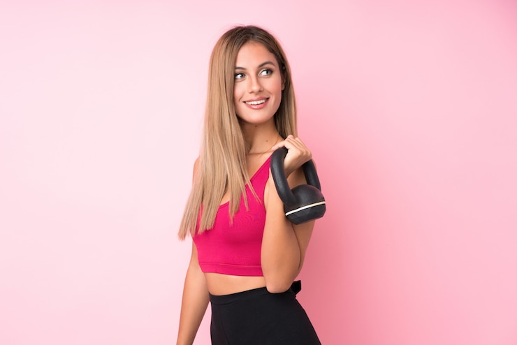 Photo femme blonde jeune sport au cours de l'haltérophilie rose isolé