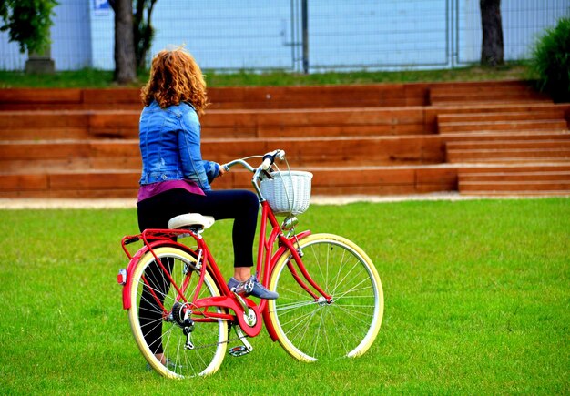 Femme blonde marchant dans le parc avec un denim bleu sur un vélo rouge