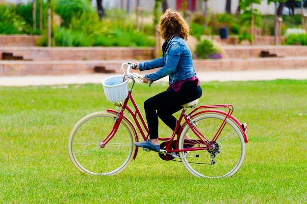 Femme blonde marchant dans le parc avec un denim bleu sur un vélo rouge