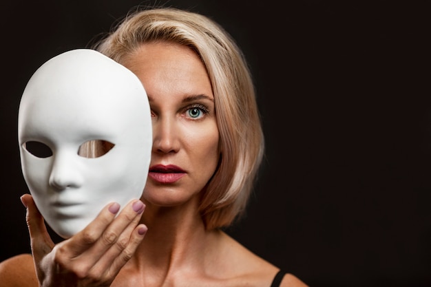 Femme blonde avec un masque blanc à la main. Fermer. Fond noir.