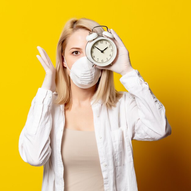 Femme blonde en masque facial et réveil sur mur jaune