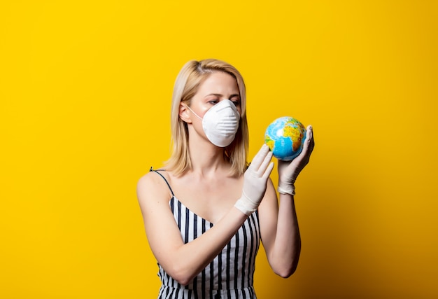 Femme blonde en masque et gants avec globe terrestre