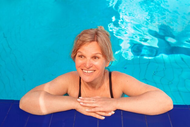 Femme blonde mature émotionnelle drôle au bord de la piscine vacances d'été et sport