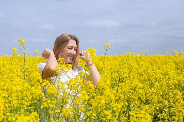 Femme blonde mature souriante en fleurs de colza jaune sur le terrain humeur d'été bonnes vacances