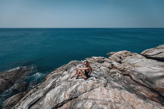 La femme blonde mince est sur la falaise par la vaste mer bleue, appréciant la marine ; paix, calme.