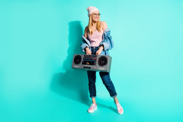 Femme blonde à la mode posant contre le mur bleu