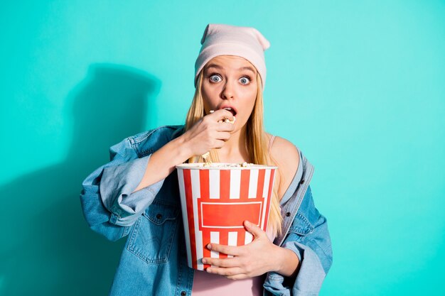 Femme blonde à la mode posant contre le mur bleu