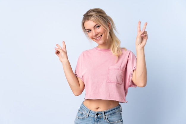 Femme blonde sur mur bleu isolé montrant le signe de la victoire avec les deux mains