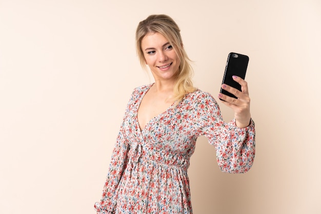 Femme blonde sur un mur isolé faisant un selfie