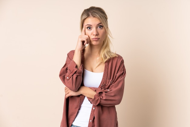 Femme blonde sur un mur isolé en pensant à une idée