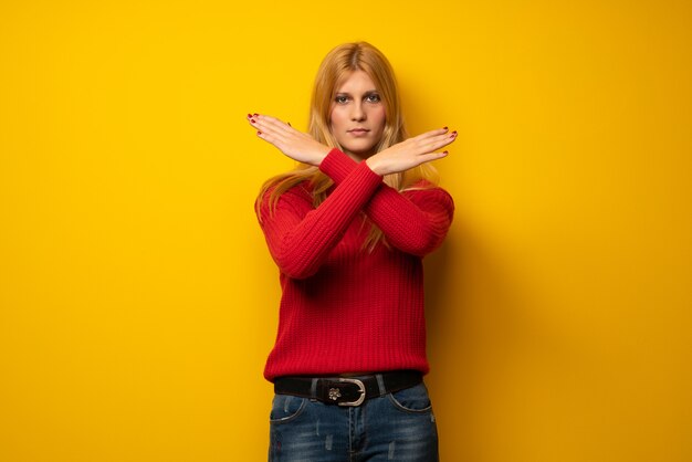 Femme blonde sur un mur jaune, envoyant un message avec le téléphone portable