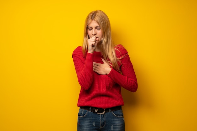 Une femme blonde sur un mur jaune souffre de toux et se sent mal