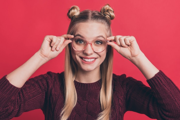 Femme blonde avec des noeuds et des lunettes posant contre le mur rouge