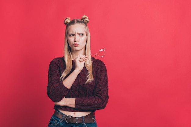 Femme blonde avec des noeuds et des lunettes posant contre le mur rouge