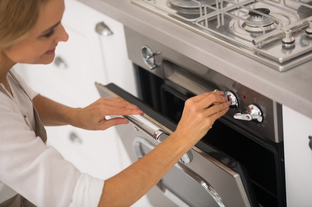 Femme blonde ouvrant le four dans la cuisine