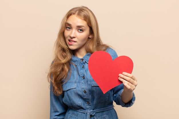 Femme blonde à la perplexité et à la confusion, mordant la lèvre avec un geste nerveux, ne sachant pas la réponse au problème