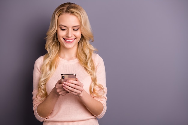 Femme blonde posant dans un pull contre le mur violet