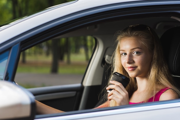 Femme blonde pose avec une tasse de papier en voiture