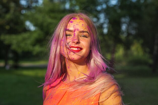 Femme blonde positive avec de longs cheveux couverts de peinture sèche violette célébrant le festival Holi