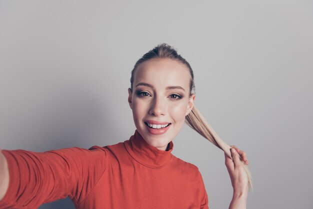 Femme blonde avec un pull à col roulé rouge posant contre le mur gris