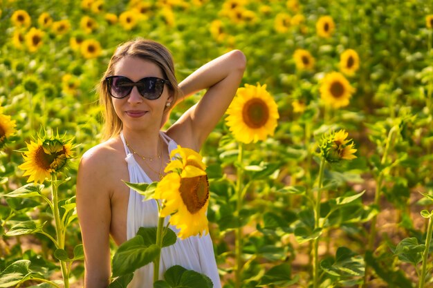 Une femme blonde de race blanche avec des lunettes de soleil et une robe blanche dans un beau champ de tournesols