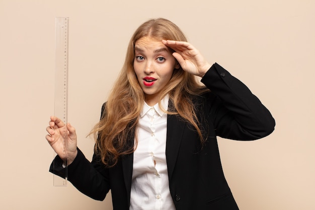 Femme blonde à la recherche de bonheur, étonné et surpris, souriant et réalisant une bonne nouvelle incroyable et incroyable