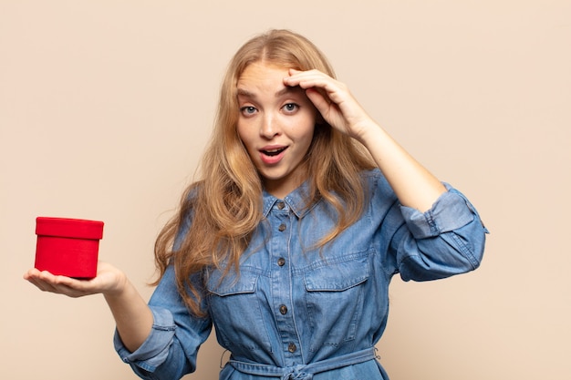 Femme blonde à la recherche de bonheur, étonné et surpris, souriant et réalisant une bonne nouvelle incroyable et incroyable