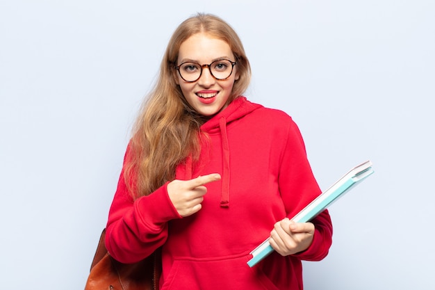 Femme blonde à la recherche excitée et surprise en pointant vers le côté et vers le haut pour copier l'espace