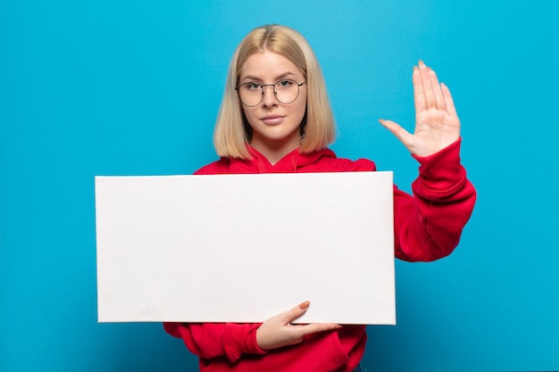 Femme blonde à la recherche sérieuse, sévère, mécontente et en colère montrant la paume ouverte faisant le geste d'arrêt