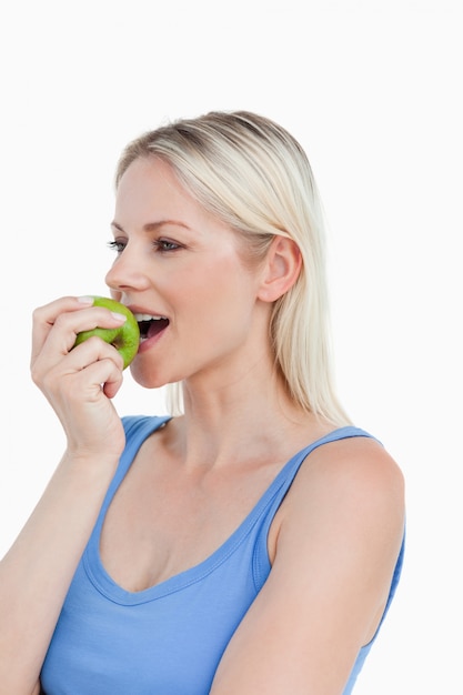 Femme blonde regardant sur le côté tout en mangeant une pomme verte