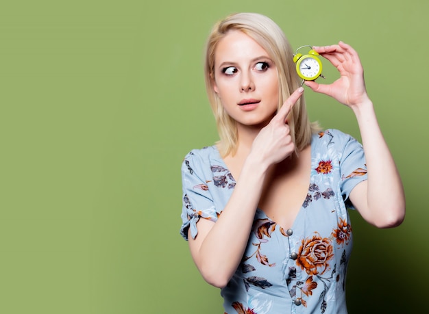 Femme blonde avec réveil sur mur vert