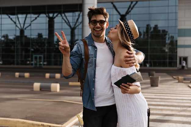 Femme blonde en robe blanche embrasse son petit ami près de l'aéroport