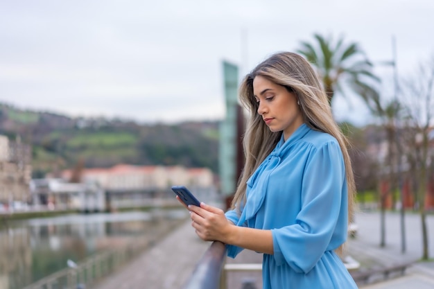 Femme blonde en robe bleue avec téléphone sur le concept de style de vie de la rivière de la ville