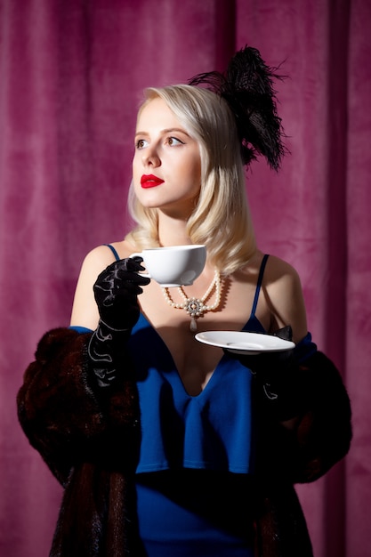 Femme blonde en robe bleue vintage et manteau de fourrure avec tasse de café