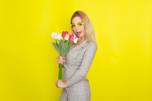 Femme blonde en robe à carreaux tenant un bouquet de tulipes