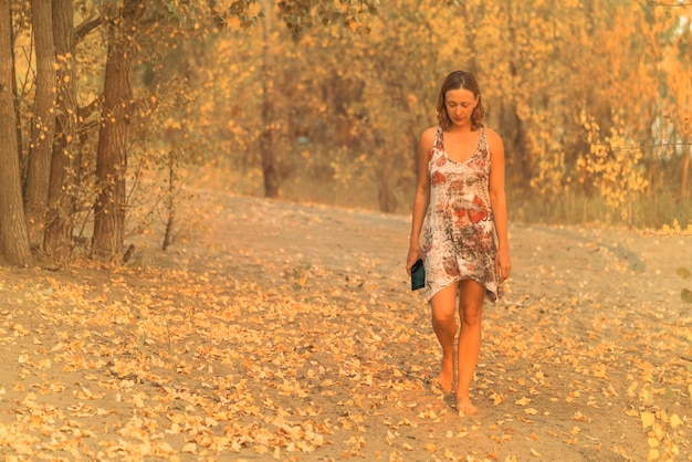 Femme blonde en robe marchant pieds nus dans la forêt d'automne