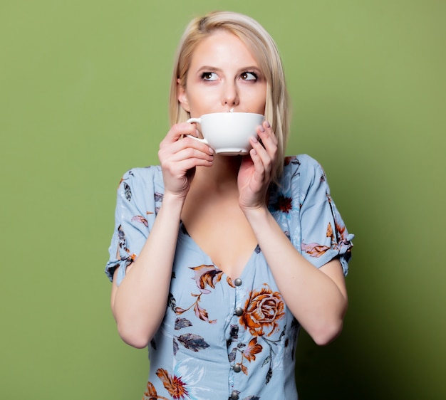 Femme blonde en robe avec une tasse de café sur le mur vert. Studio tourné isolé