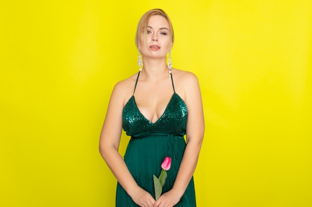 Femme blonde en robe verte tenant une tulipe rose
